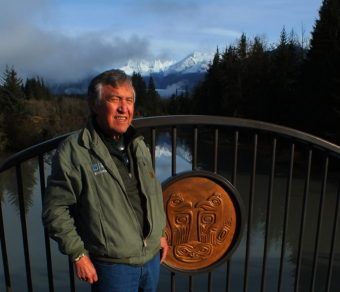 Roy Peratrovich Jr. stands next to one of the bronze medallions he designed for the first Brotherhood Bridge created in 1965. The medallions were recovered, restored and installed on the new Brotherhood Bridge that was dedicated Oct. 24, 2015. (Photo by Matt Miller/KTOO)