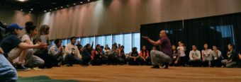Xeetli.eesh Lyle James, a group leader for the Woosh.ji.een dancers in Juneau, teaches a small crowd of young people during a break out session at the Elders and Youth Conference in Anchorage. (Photo by Jennifer Canfield/KTOO)