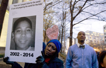 In a photo taken Dec. 1 of last year, Tomiko Shine holds up a picture of Tamir Rice during a protest. It has been nearly a year since then, but a grand jury has not reached a decision on the case. Jose Luis Magana/AP