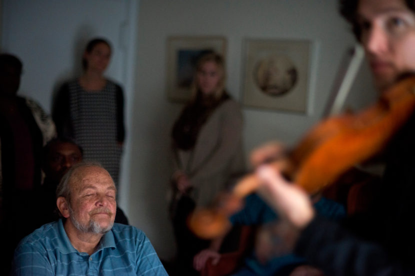 Wall (left) listens to violinist Fain perform during the Make Room concert at Wall's apartment in Annapolis, Md. The concert is a fundraiser to help Wall pay his rent and shine a light on the growing lack of affordable housing. Brandon Chew/NPR