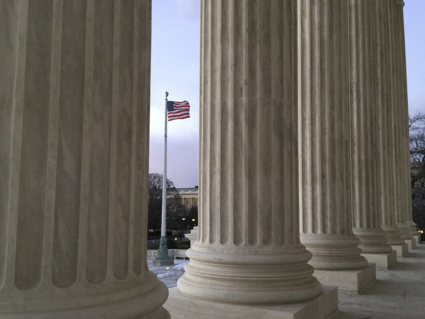 The American flag, seen through the columns of the Supreme Court building, blows in the wind on Feb. 13. (Jon Elswick/AP)