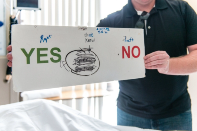 Jeremy Wilson communicates with his father using a makeshift board at St. John’s Pleasant Valley Hospital on February 24, 2016. His father, John Wilson, can’t speak but can communicate using his eyes. (Heidi de Marco/KHN)