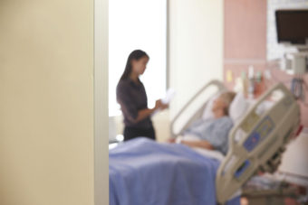 Focus On Hospital Room Sign With Doctor Talking To Patient. Photo from Kaiser Health News.