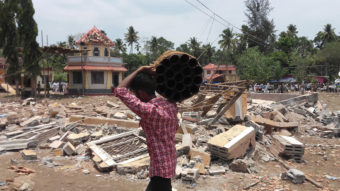A man carries empty fireworks shells past a collapsed building after a massive fire broke out during a fireworks display at a temple complex in Paravoor village in the state of Kerala, India. AP