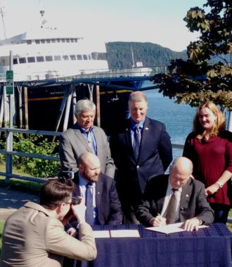 Gov. Bill Walker signs a memorandum of understanding with the Southeast Conference as its President, Gary White, Lt. Gov. Byron Mallott and Transportation Commissioner Marc Luiken watch Thursday at the Auke Bay Ferry Terminal. (Photo by Ed Schoenfeld/ CoastAlaska News)
