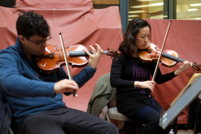Vega String Quartet members Domenic Salerni and Jessica Shuang Wu play violin at the State Office Building Atrium during a Brown Bag Concert as part of the Juneau Jazz & Classics Festival on Monday, Mar. 9. (Photo by Annie Bartholomew/KTOO)