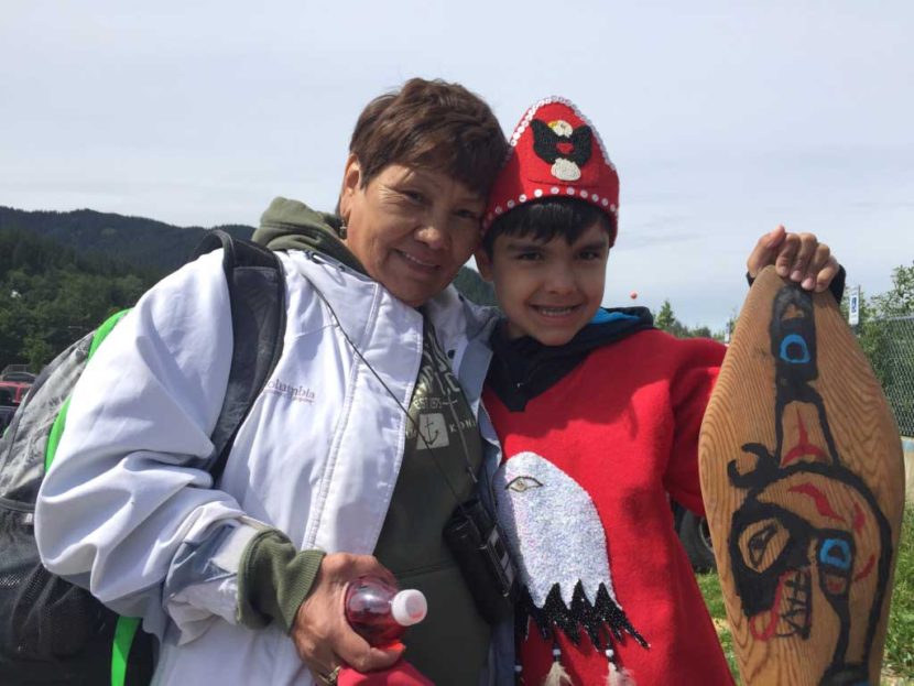 Marie Johnson greets her 10-year-old grandson, Roary Earl Bennett, who just completed a 3-day paddle from Coghlan Island to Douglas for Celebration 2016. Johnson made Bennett's tunic out of felt and abalone shells. (Photo by Emily Kwong/KCAW)