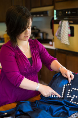 Designer Lily Hope creates a wave basketry design in buttons on a silky blue dress for Celebration's Native Fashion Show. (Photo by Annie Bartholomew/KTOO)