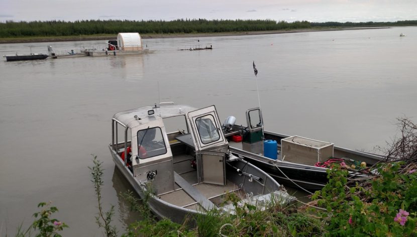 The hydrokinetic turbine being tested by UAF in Nenana is suspended into the Tanana River from the middle of three platforms, at left. The bouy in the upper right marks the point where the barges are anchored to the river bottom. The debris diverter is located between the bouy and barges. (Photo by Tim Ellis/KUAC)