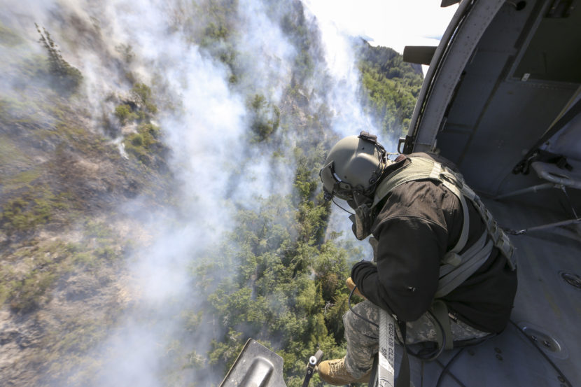 Staff Sgt. Steven Elliot, a crew chief with B Co., 1st Battalion, 207th Aviation Regiment, looks onto the McHugh Creek Fire during operations in support of wildfire suppression efforts near Anchorage, July 20, 2016. (Public domain photo by Staff Sgt. Balinda O’Neal Dresel/U.S. Army National Guard)