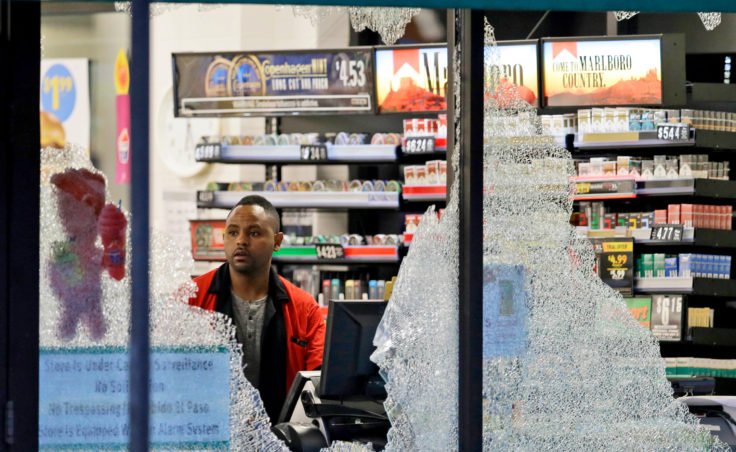 A clerk looks through broken windows, which were shot out at a convenience store in downtown Dallas. (Photo by LM Otero/AP)