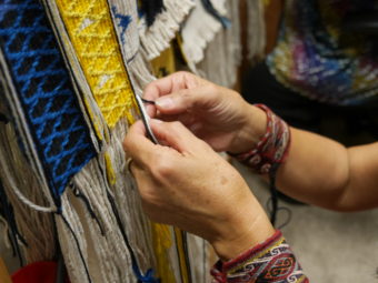 Clarissa Rizal's fingers dexterously manipulate the various colors of yarn Monday afternoon, August 22, 2016, as she works on the side borders of the Weavers Across Waters Chilkat/Ravenstail community robe. Rizal estimates that it takes her an hour to weave one inch of the side border, which means the robe is incredibly time intensive. (Photo by Tripp J Crouse/KTOO)