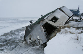 An abandoned house at the west end of Shishmaref, Alaska, sits on the beach after sliding off during a fall storm in 2005. (Photo by Diana Haecker/Associated Press)