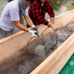 Jerrod Galanin gets help lowering a basket of hot lava rocks into the canoe. (Photo by Emily Russell/KCAW)