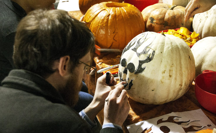 Sam Bornstein uses pins to apply a pattern to his pumpkin. Bornstein drew his design on paper, cut it out and then used it as a stencil to carve his pumpkin at Juneau Makerspace in Lemon Creek. (Photo by Tripp J Crouse/KTOO)