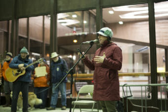 A woman in a red jacket and blue had speaks at a rally outside the Juneau Federal Building