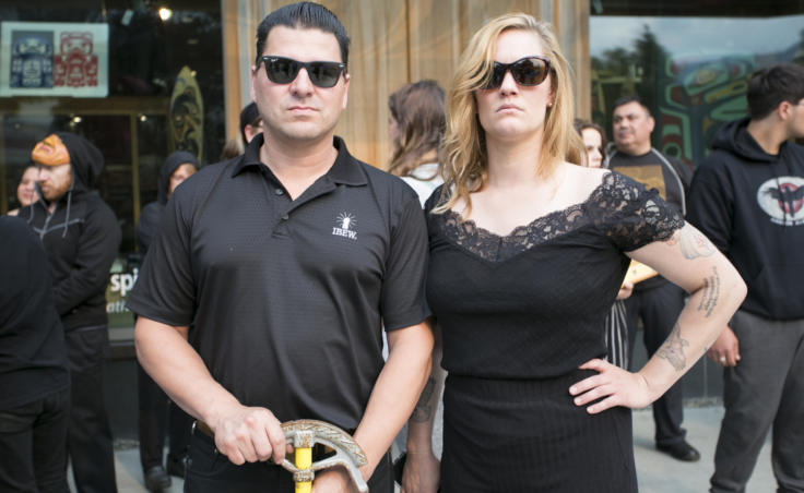 A man and woman wearing black stand on the street Assistant Business Manager for the International Brotherhood of Electrical Workers Local 1547 union and Juneau performance artist Rachel Byrd stand outside Sealaska Heritage Institute at the demonstration and public art "black out" on Tuesday, July 9, 2019. (Photo by Annie Bartholomew/KTOO)