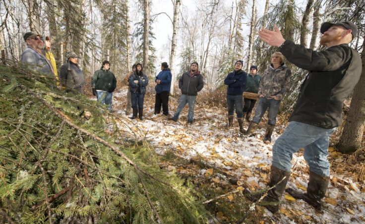 Kaleb Franke, at right, talks about how to build an emergency shelter, like one he constructed at left, as campers listen in a wooded area near Spirit Lake in Kenai, in October 2016. (Photo by Scott Moon/Kenaitze Indian Tribe)