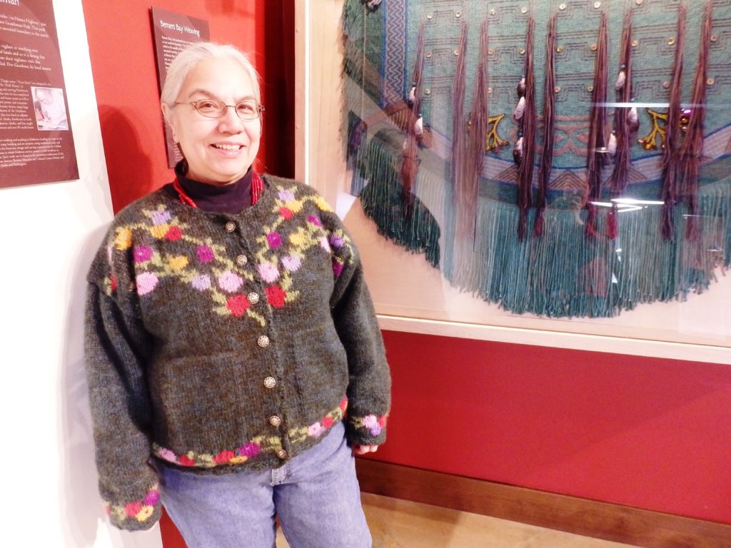 Lani Hotch, executive director of the Jilkaat Kwaan Heritage Center, stands next to her contemporary weaving that represents Berners Bay. (Photo by Emily Files/KHNS)