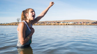 Stephanie Jasper holds up her fist and yells while protesting in the Cannonball River during a standoff with police at Turtle Island, north of the Standing Rock Sioux Reservation. (Photo by Emily Kask for NPR)