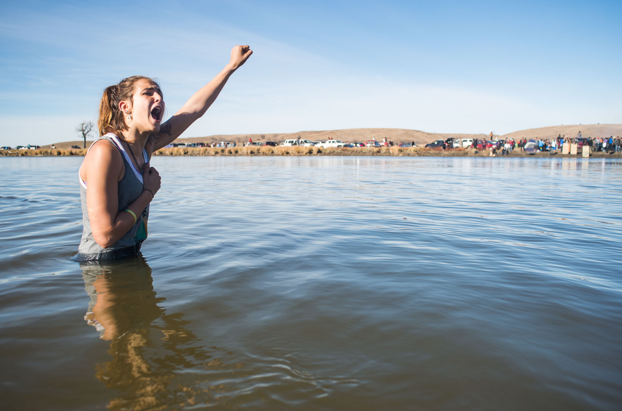 Stephanie Jasper holds up her fist and yells while protesting in the Cannonball River during a standoff with police at Turtle Island, north of the Standing Rock Sioux Reservation. (Photo by Emily Kask for NPR)