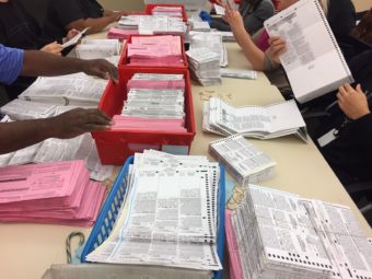 Election workers sort through unprocessed vote-by-mail ballots at the Sacramento County Registrar of Voters office on Monday. (Photo by Ben Adler/Capital Public Radio)