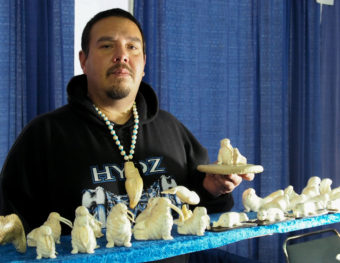 Dennis Pungowiyi shows off one of his favorite carving motifs, a mother walrus with her pup. (Photo by Zachariah Hughes/Alaska Public Media)