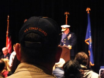 A Boy Scout troop leader, wearing a cap with U.S. Coast Guard embroidered on the back, listens as Rear Adm. Michael McAllister, commander of the U.S. Coast Guard's 17th District, speaks during Friday's Veterans Day observance at Centennial Hall.