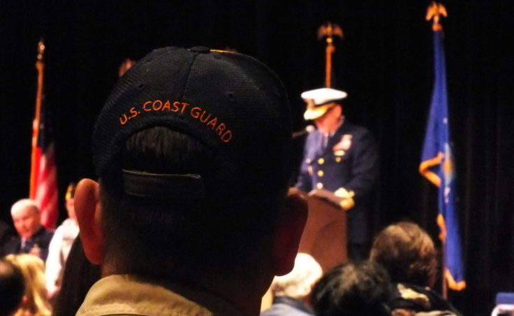A Boy Scout troop leader, wearing a cap with U.S. Coast Guard embroidered on the back, listens as Rear Adm. Michael McAllister, commander of the U.S. Coast Guard's 17th District, speaks during Friday's Veterans Day observance at Centennial Hall.