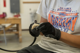 A student uses a with a dremel tool to shape her fish carving. Master ivory carver Jerome Saclamana taught students in Nome the tradition in August 2015. (Photo by Mitch Borden, KNOM)