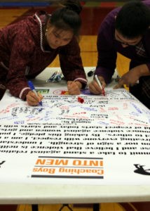 Two student wrestlers sign the poster after completing the ‘Coaching Boys into Men’ program. (Emily Russell/KCAW)