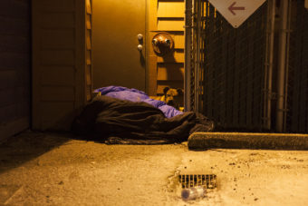Two people and a dog curl up near a boiler room on Shattuck Way on Jan. 20, 2017, in downtown Juneau, Alaska. (Photo by Rashah McChesney/Alaska's Energy Desk)