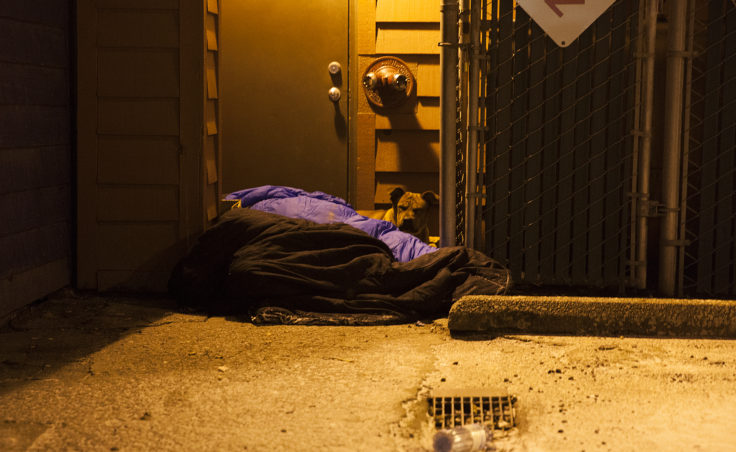 Two people and a dog curl up near a boiler room on Shattuck Way on Jan. 20, 2017, in downtown Juneau, Alaska. (Photo by Rashah McChesney/Alaska's Energy Desk)