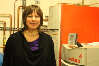 Christal Higdon with wood pellet boiler (Photo by Elizabeth Jenkins/Alaska's Energy Desk)