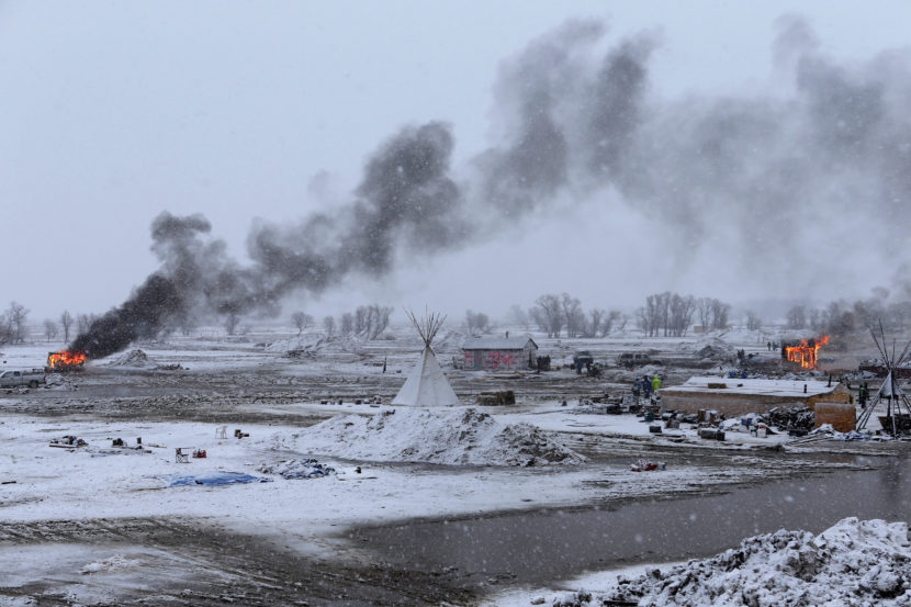 Snow falls on the Oceti Sakowin camp on Monday as structures smolder. (Photo by Angus Mordant for NPR)