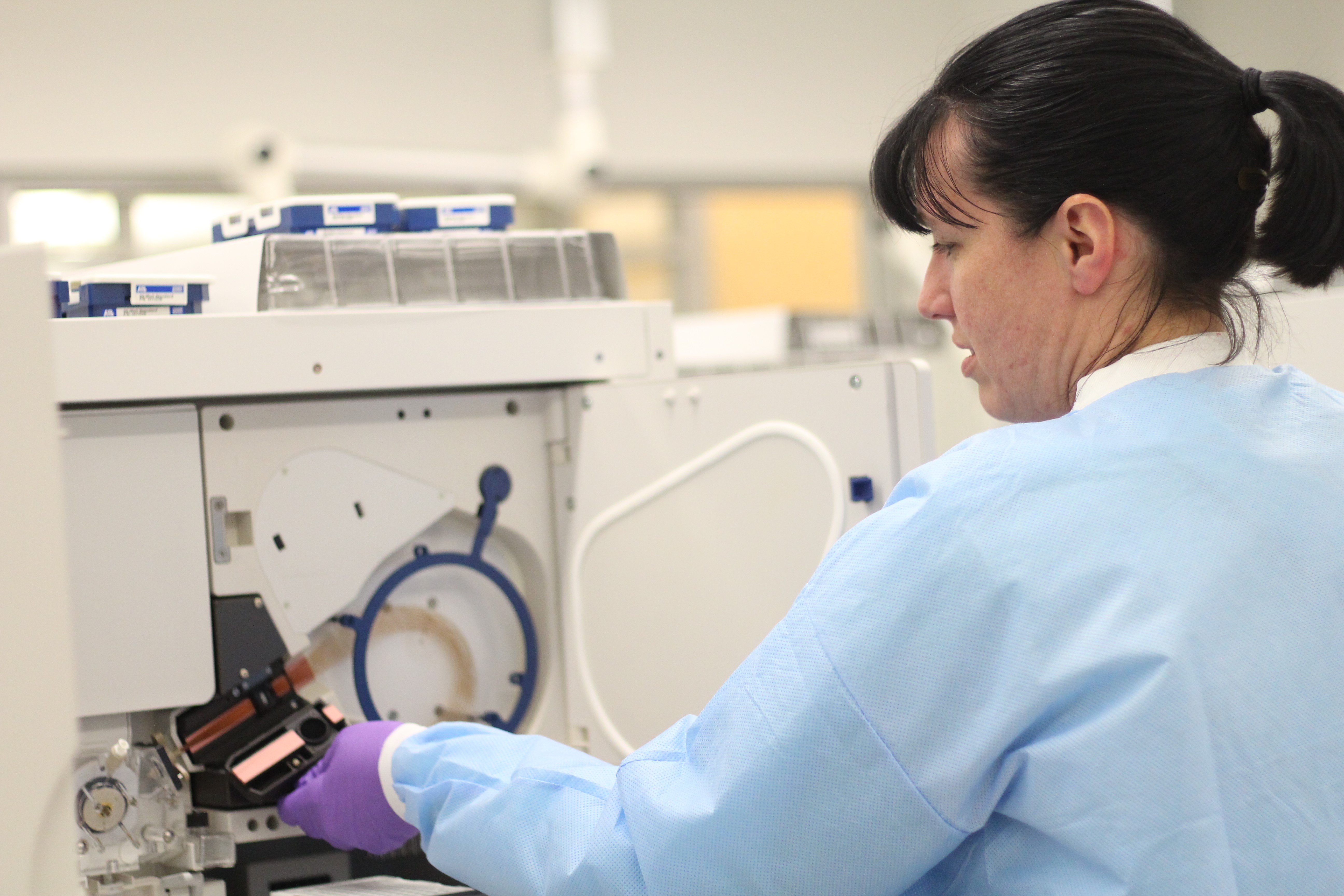 Michelle Collins demonstrates how to use one of the machines that processes DNA samples. (Photo by Anne Hillman/Alaska Public Media)