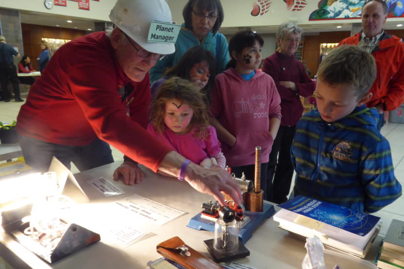 Bill Leighty, the Planet Manager shows a group of kids his model steam engine at the Juneau Renewable Fair in the JDHS commons on Earth Day.