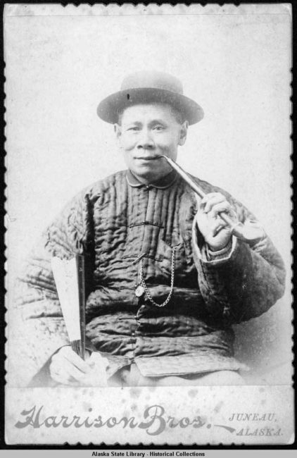 China Joe smokes a pipe and holds a fan in this gold rush era studio portrait.