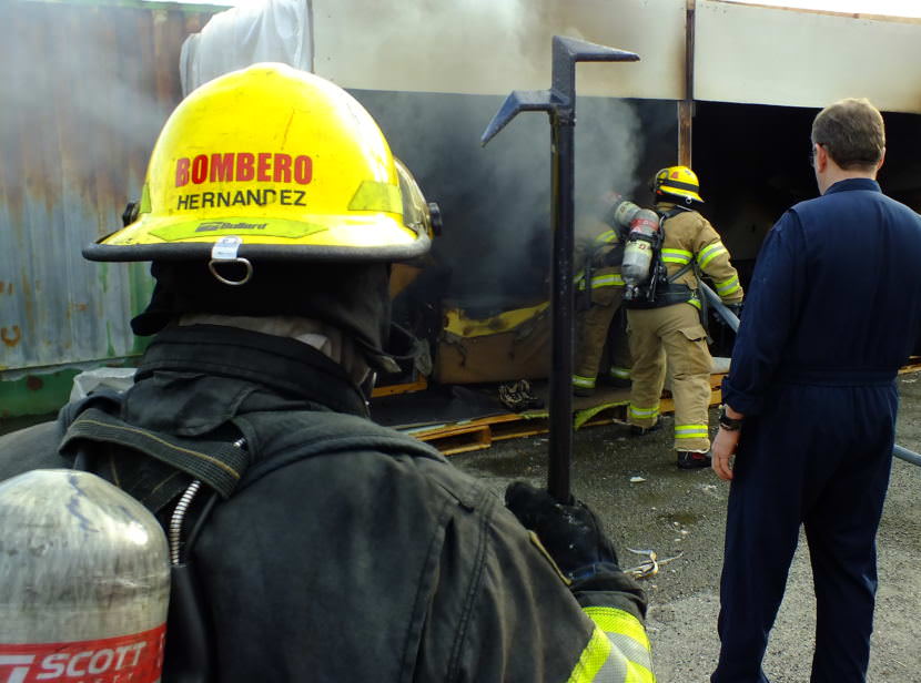 Instructor Ernie Misewicz (right) watches as firefighters with Capital City Fire/Rescue put out a fire in one of the staged rooms during a recent fire investigator training exercise at Juneau’s Hagevig Regional Fire Training Center. (Photo by Matt Miller/KTOO)