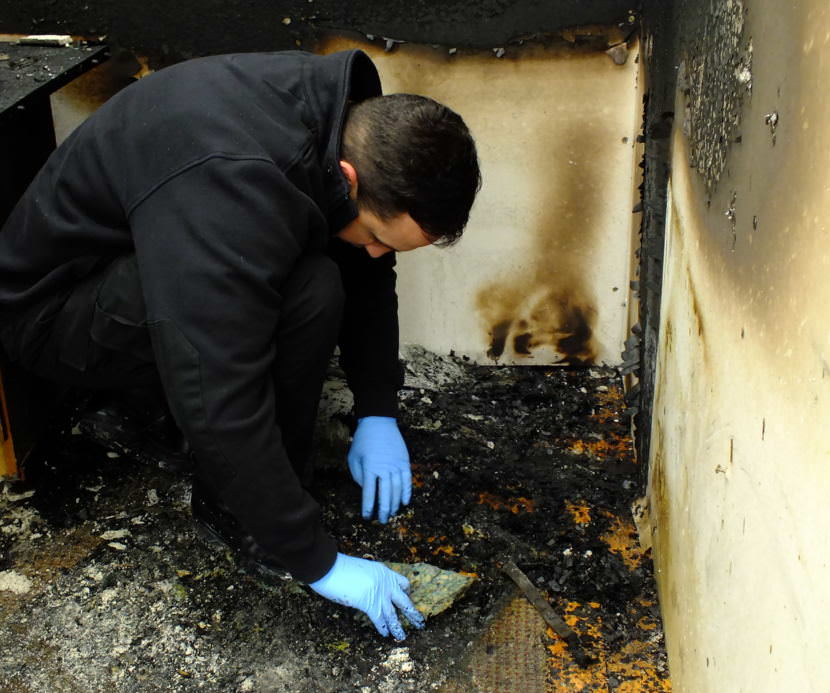 A student investigator sifts through debris and checks the underside of a carpet for a possible accelerant during a recent fire investigator training exercise at Juneau’s Hagevig Regional Fire Training Center. (Photo by Matt Miller/KTOO)