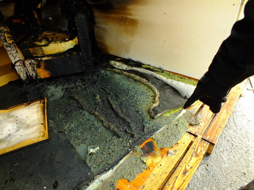 Instructor Jason Mardirosian points to the possible origin of a fire during a recent fire investigator training exercise at Juneau’s Hagevig Regional Fire Training Center. The ‘trail’ of burned and melted carpet and padding that leads to the chair indicates the possible use of a liquid accelerant. (Photo by Matt Miller/KTOO)