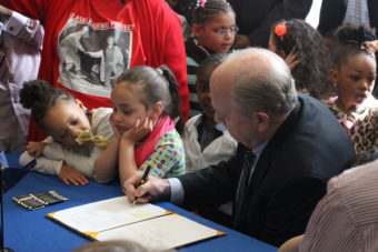 Gov. Bill Walker signs the first half of his name on SB 46 on Sunday at Shiolh Baptist Church in Anchorage, (Photo by Wesley Early/Alaska Public Media)