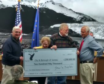 Whale Committee members Jim Clark, left, Jean Overstreet and Bruce Botelho present an oversize check for $250,000 to Mayor Ken Koelsch to help fund the infrastructure for the whale statue at the June 5, 2017 meeting of the Juneau Assembly. (Photo by Jacob Resneck/KTOO)