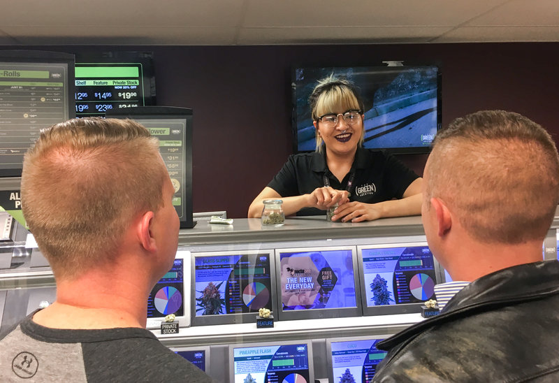 Yessenia Hinojos, a budtender at a Denver cannabis dispensary called The Green Solution, describes marijuana strains to A.J. Tarantino (left) and Philip Gurley. Both men are officers with Colorado State Patrol.