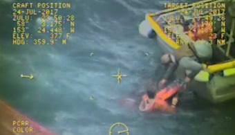 Captain with crewman in water in the process of helping man onto vessel. Screencap from video by Air Station Kodiak