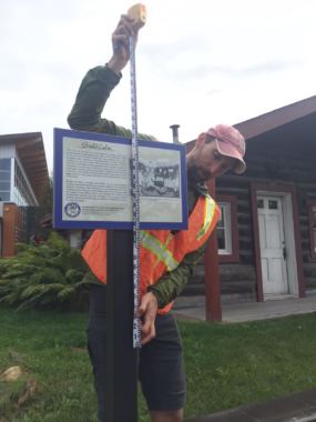 National Weather Service hydrologist Ed Plumb takes a measurement for installation of high water mark sign on an historic cabin near the Morris Thompson Center. (Photo by Dan Bross/KUAC)