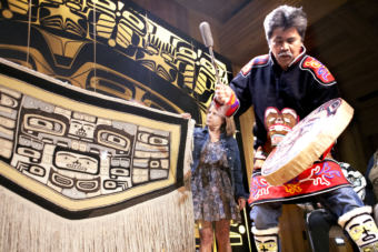 Yeilnaau Joe Zuboff calls for the spirits of a 100-plus-year-old Chilkat robe to return home Aug. 26, 2017, during a homecoming ceremony in the Shuka Hit clan house in downtown Juneau's Walter Soboleff Building. Gretchen Jacobsen, who with her husband donated the robe to Sealaska Heritage Institute, watches as Brian Katzeek dances behind the robe.