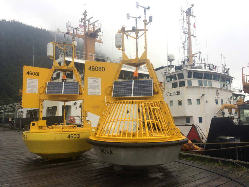 NOAA ocean and weather monitoring buoys sit on the dock at Coast Guard Station Juneau with the Canadian Coast Guard vessel Bartlett visible in the background. (Photo by Matt Miller/KTOO)
