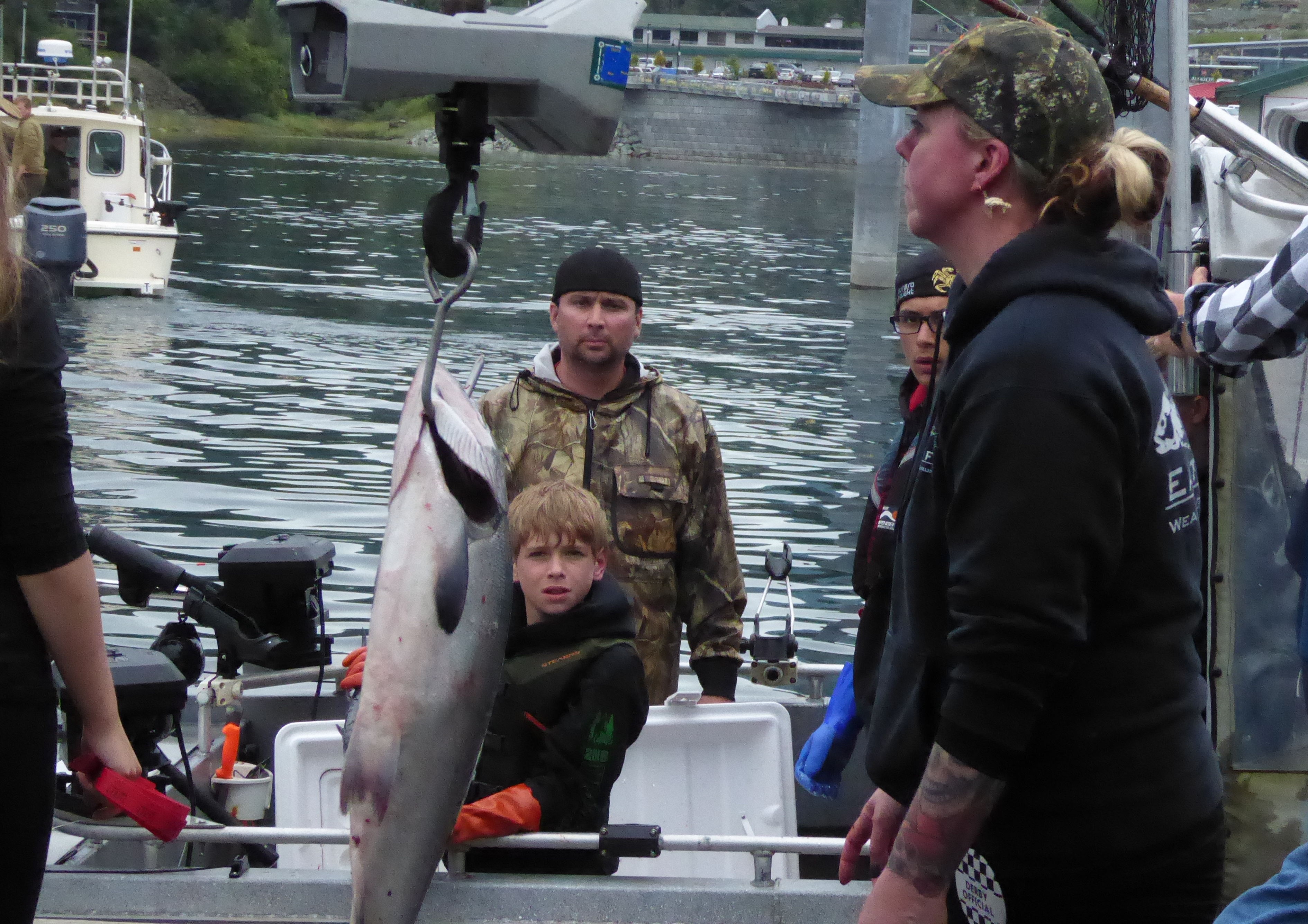 A boy and his father watch from their boat as Kami Bartness weighs their fish on a hanging scale at the Auke Bay harbor.