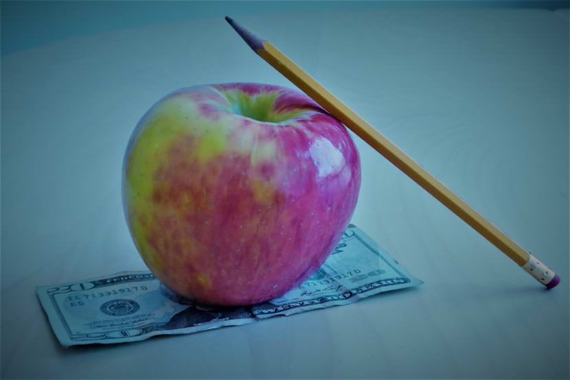 A pencil leaning against an apple sitting on top of a twenty dollar bill.